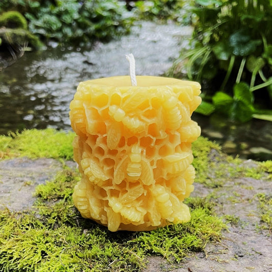 Golden beeswax pillar with deep honeycomb texture and raised bees on moss-covered stone.