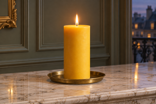 Golden 3x6-inch beeswax pillar in an antique-brass candle plate on marble in an elegant room at dusk.