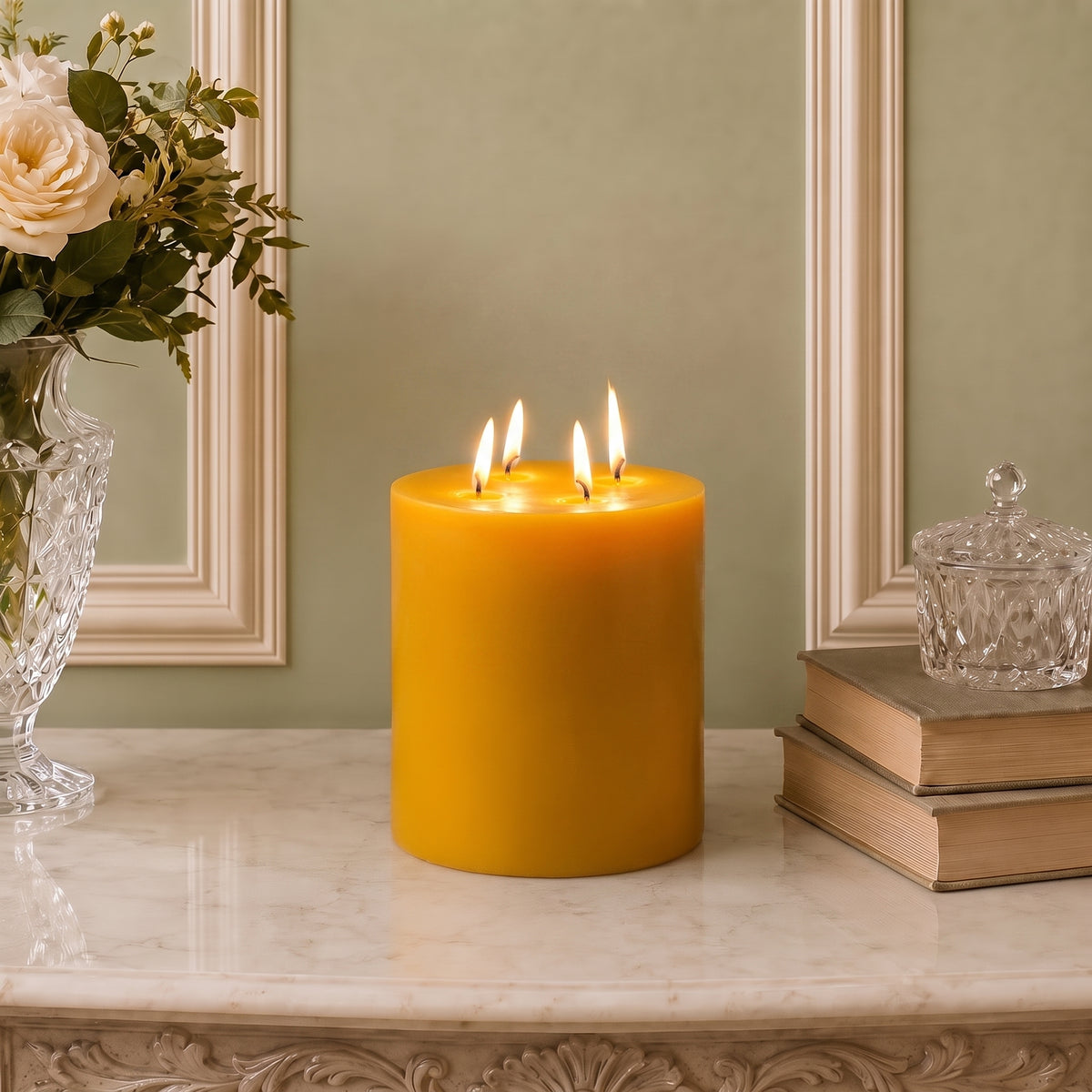 Tall golden four-wick beeswax pillar beside a crystal dish and stacked books.