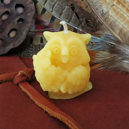 Small golden owl candle with wide eyes and feather detail, displayed with books and a feather.